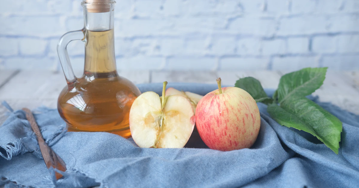Bottle of apple cider vinegar beside sliced apples